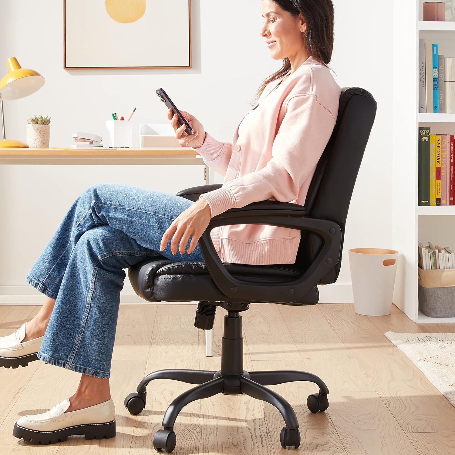 Woman sitting comfortably on a black ergonomic office chair with cushioned seat and adjustable armrests