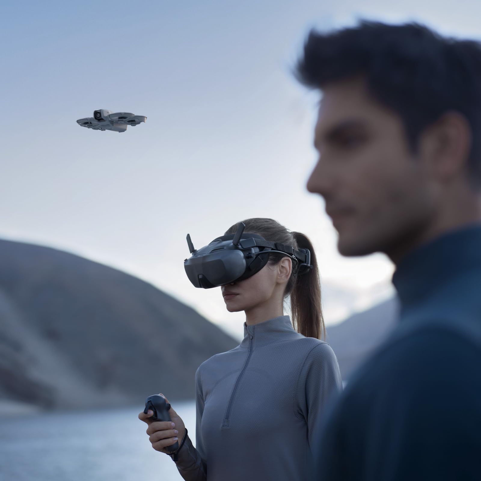 Woman using VR headset and remote to control DJI Neo mini drone 4K UHD flying outdoors near lake