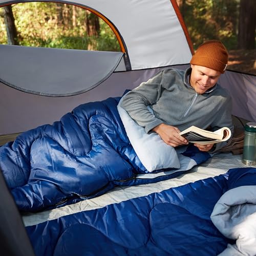 Man reading inside a dome camping tent with rainfly on a blue sleeping bag during a forest camping trip