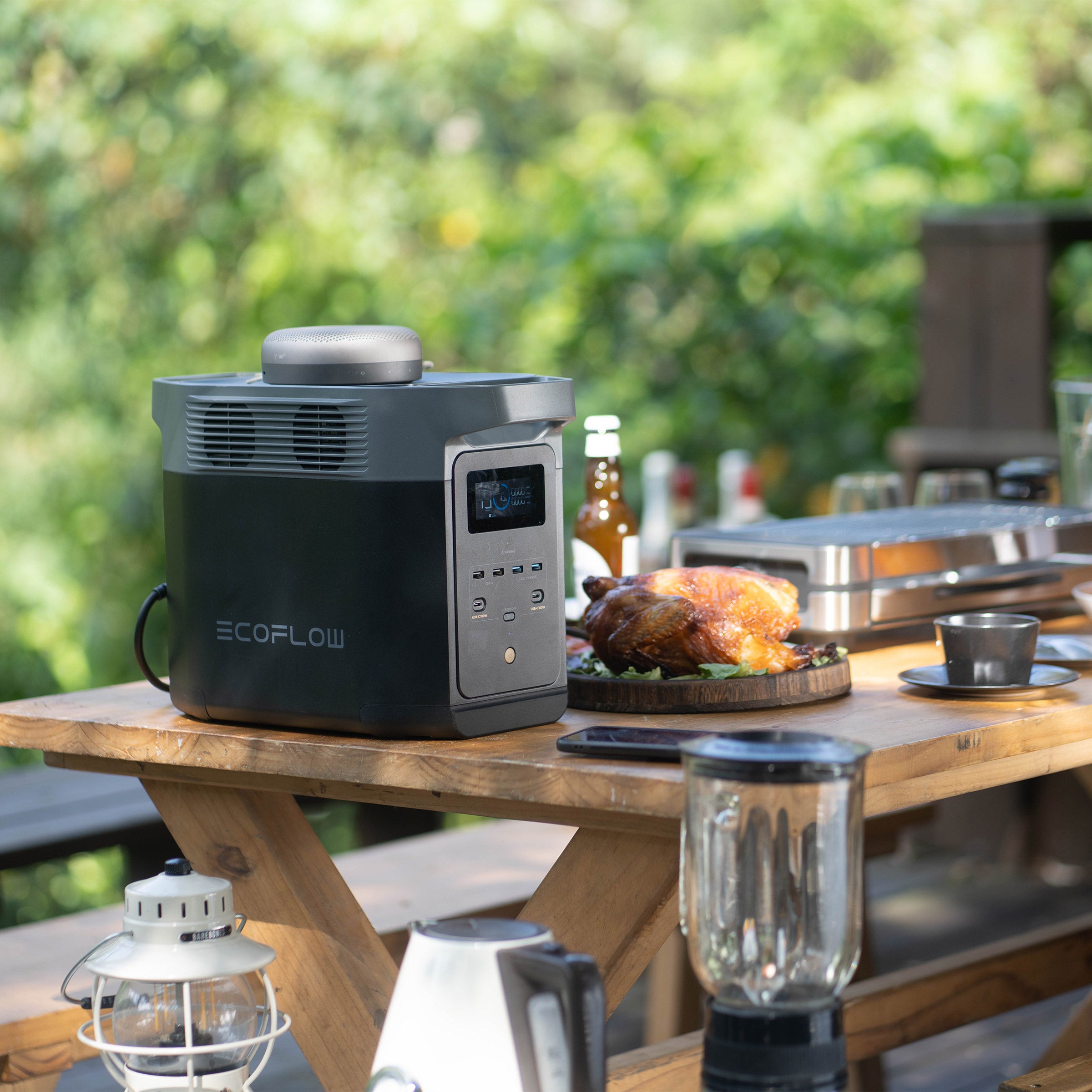 EcoFlow portable solar generator kit on wooden picnic table with roasted chicken and outdoor kitchen setup