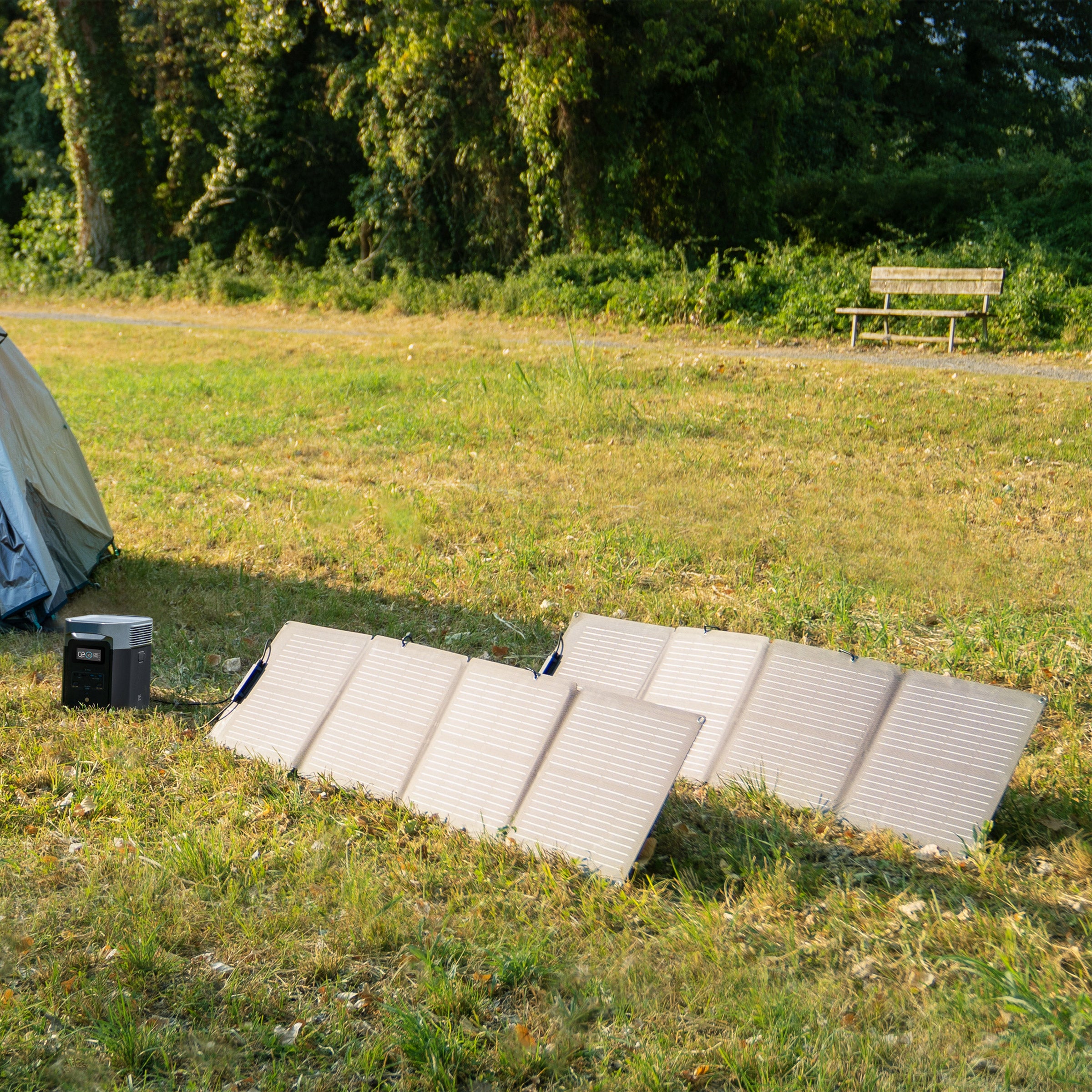 Portable solar generator kit with foldable solar panels and power station set up on grass near a tent