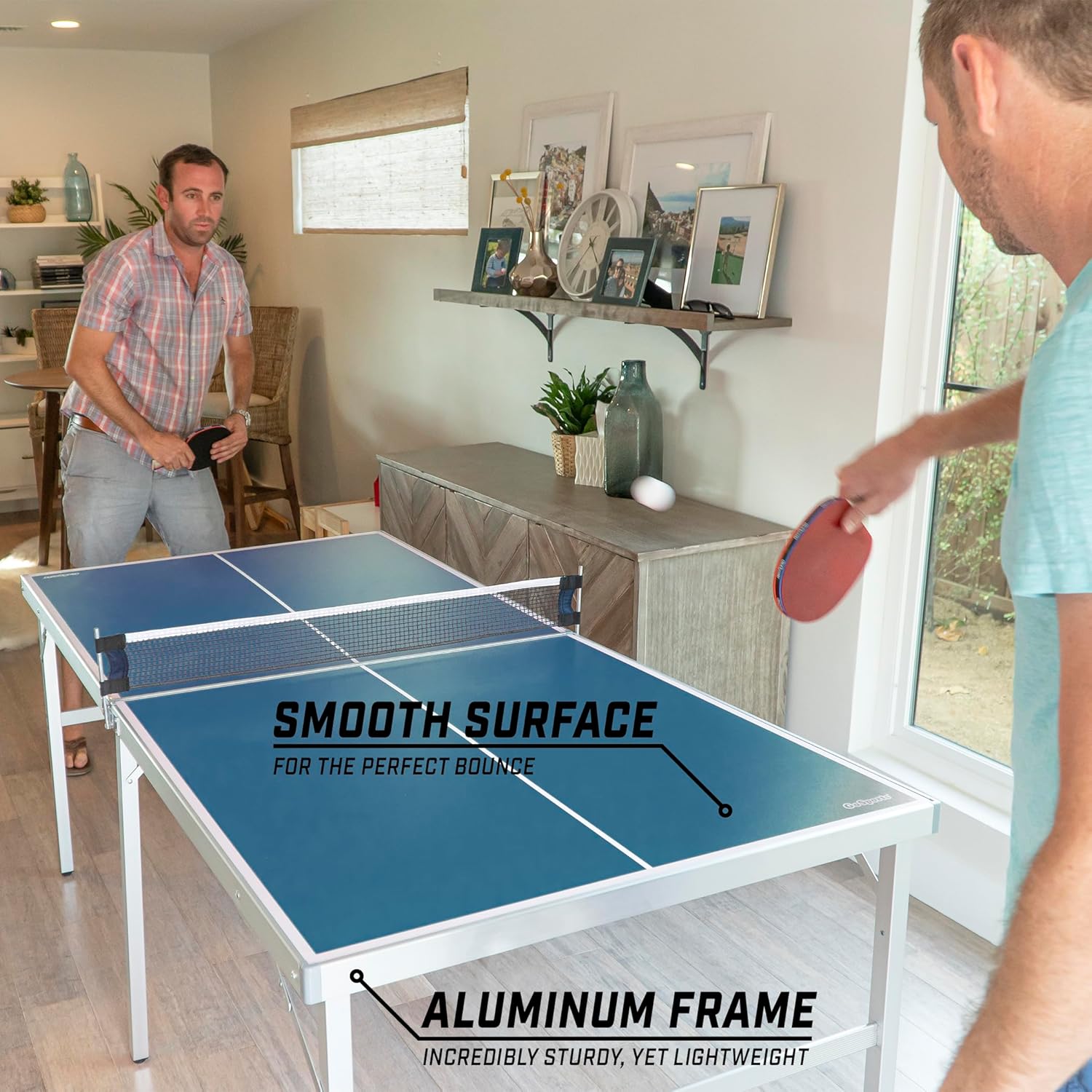 Two men playing on a portable table tennis set with a smooth blue surface and aluminum frame indoors