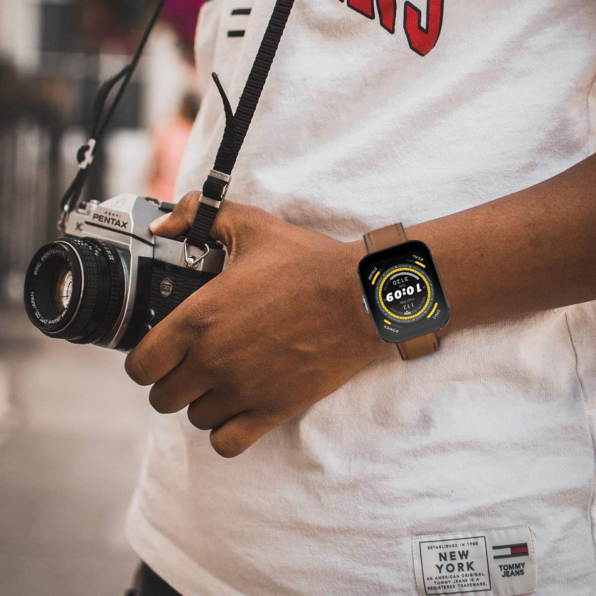 Person wearing a smartwatch with a brown ID208 plus watch band replacement while holding a vintage Pentax camera