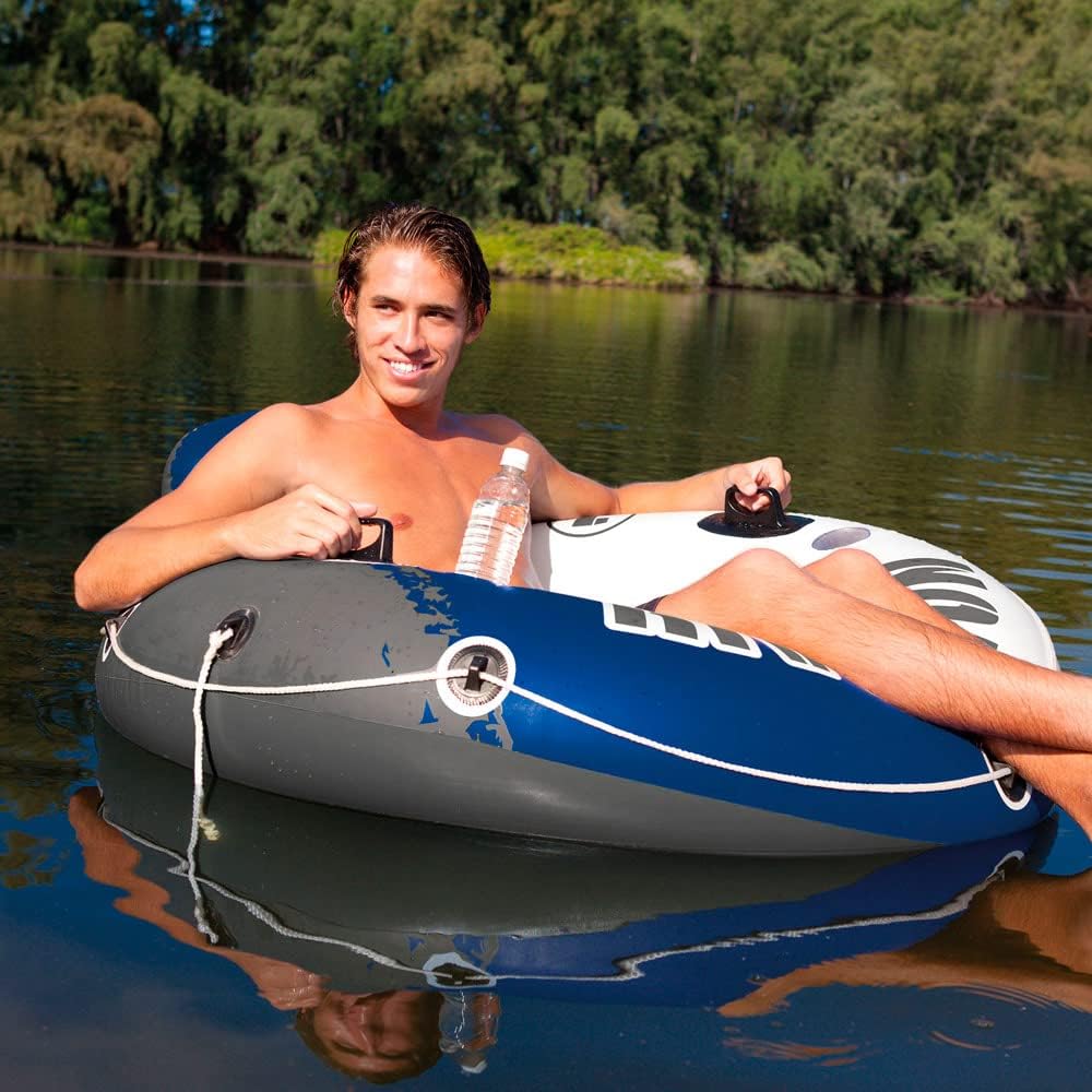 Man relaxing on a blue and gray inflatable river float for adults on calm water with trees in the background