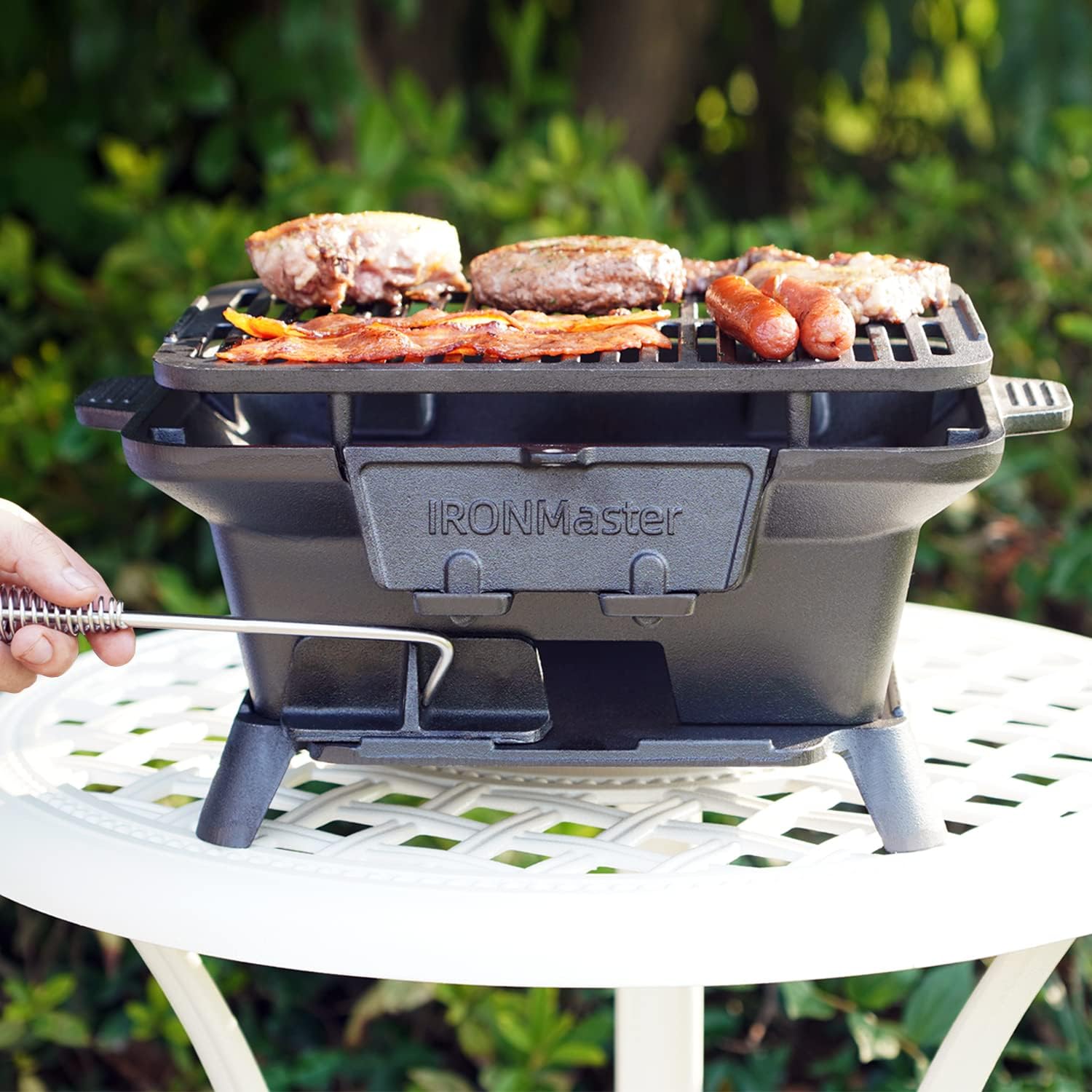 Portable cast iron bbq grill with burgers and sausages cooking on black IRONMaster grill outdoors
