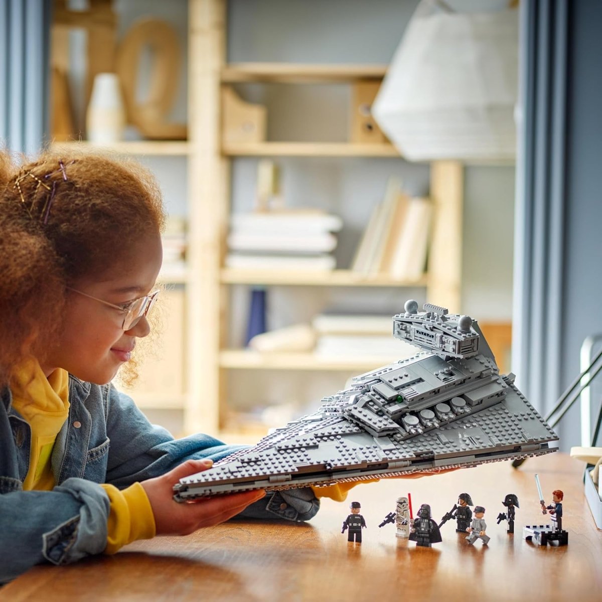 Child playing with LEGO Star Wars Imperial Star Destroyer set and minifigures on wooden table