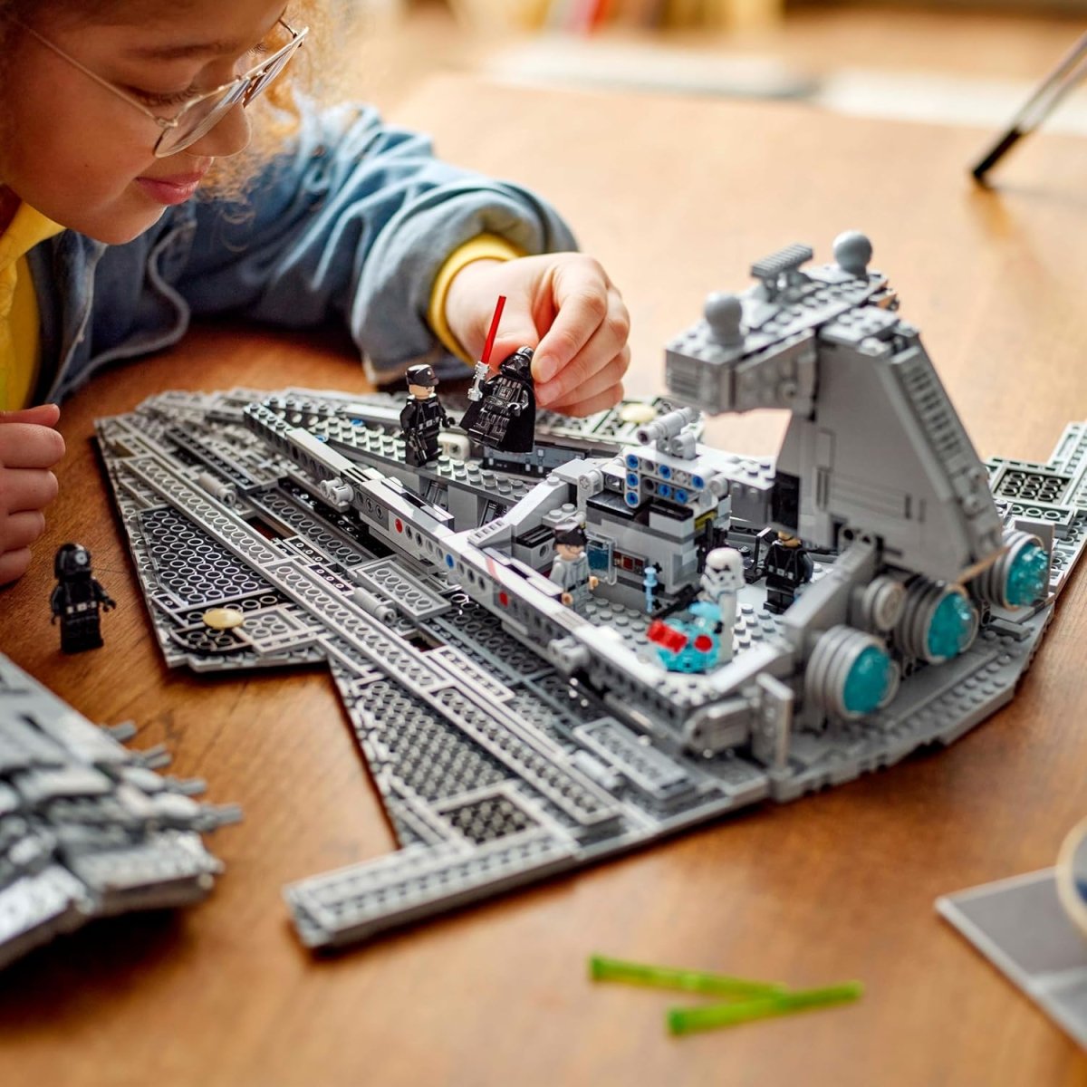 Child assembling LEGO Star Wars Imperial Star Destroyer set with detailed minifigures on wooden table