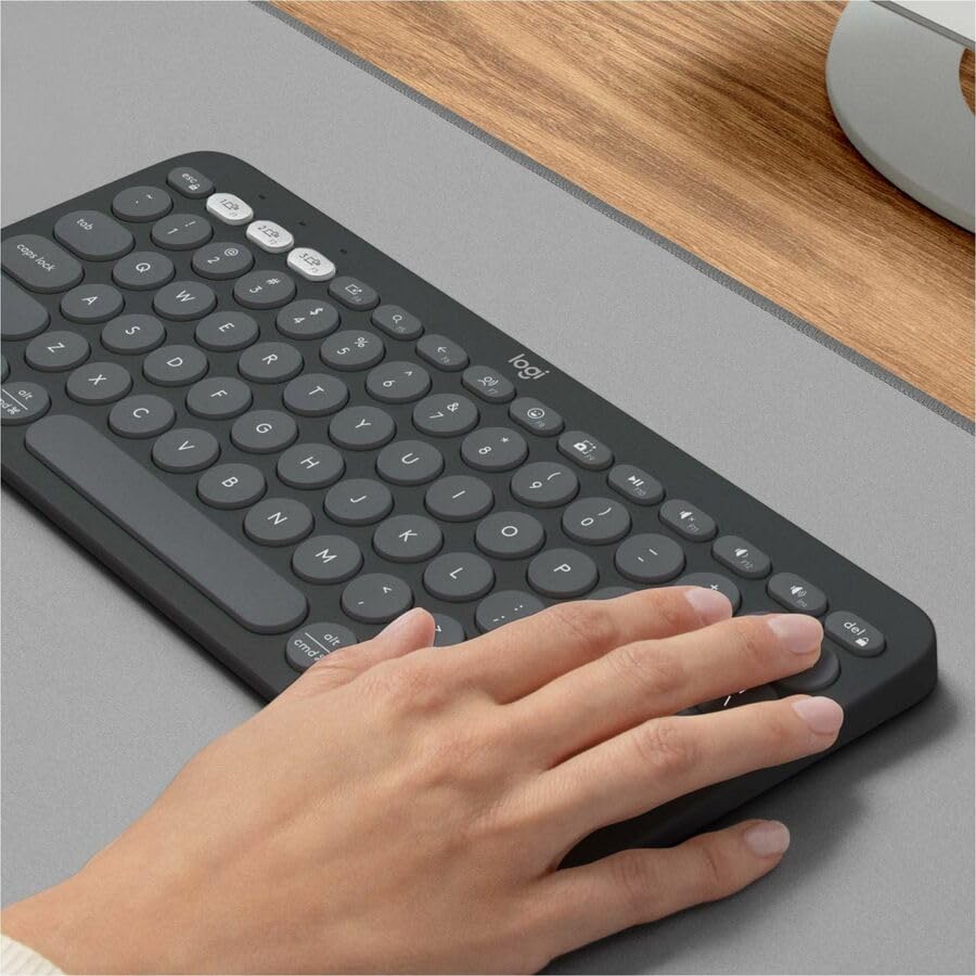 Logitech Pebble Keys 2 K380s wireless keyboard in black with round keys and hand typing on gray desk
