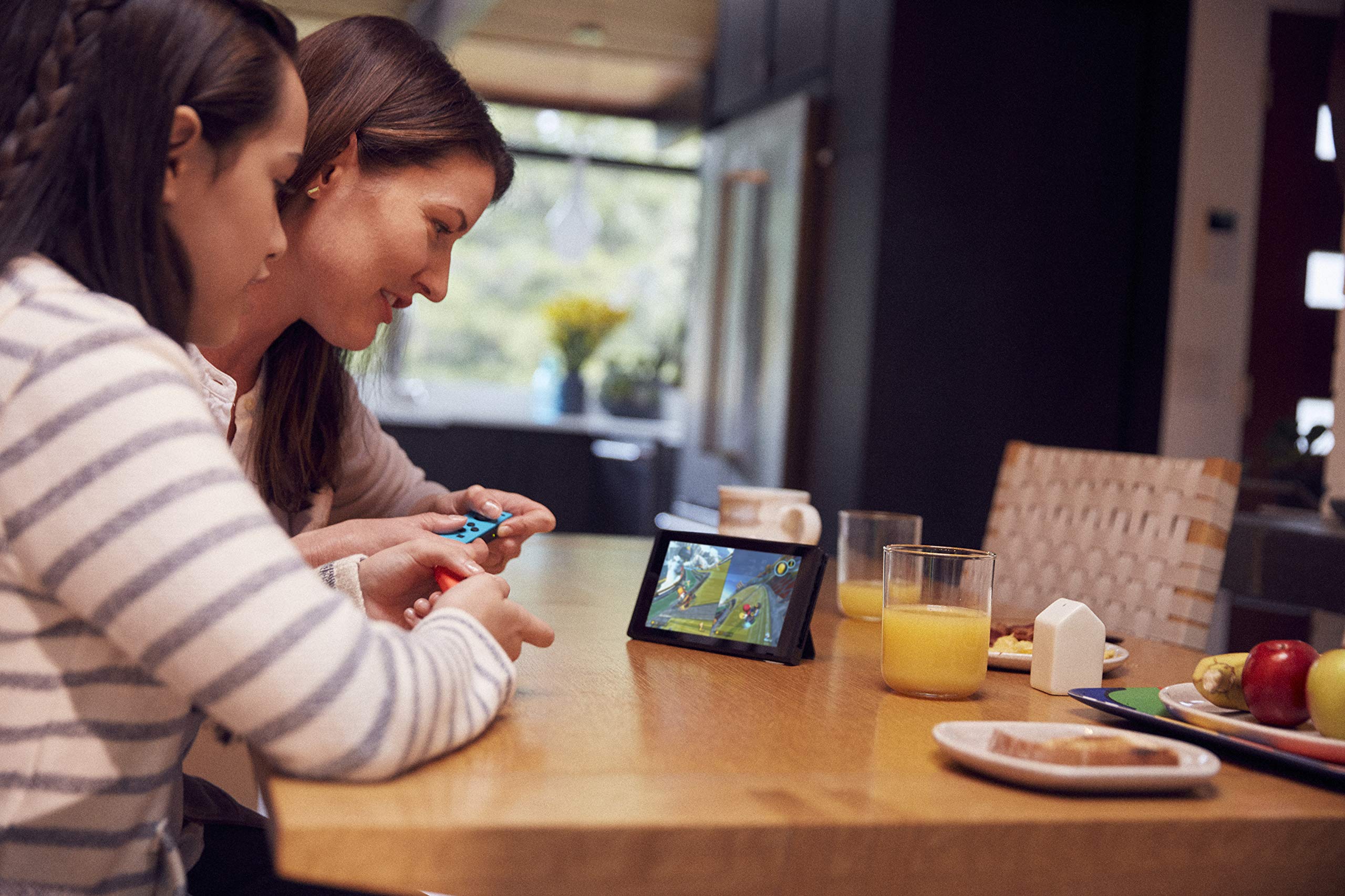 Two women playing Mario Kart 8 Deluxe Nintendo Switch on a tabletop in a cozy home setting