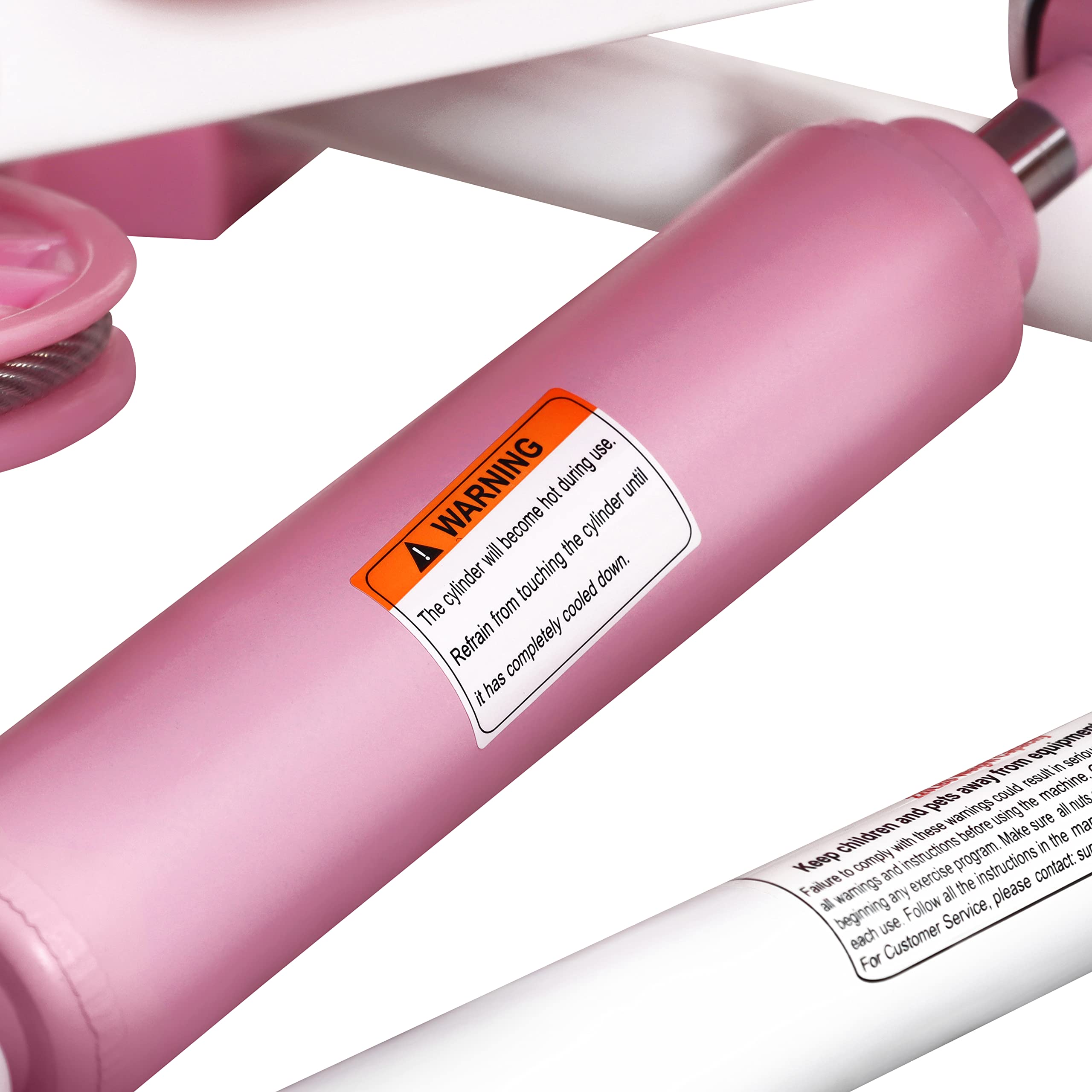 Close-up of pink hydraulic cylinder with warning label on mini stepper for home use by craques