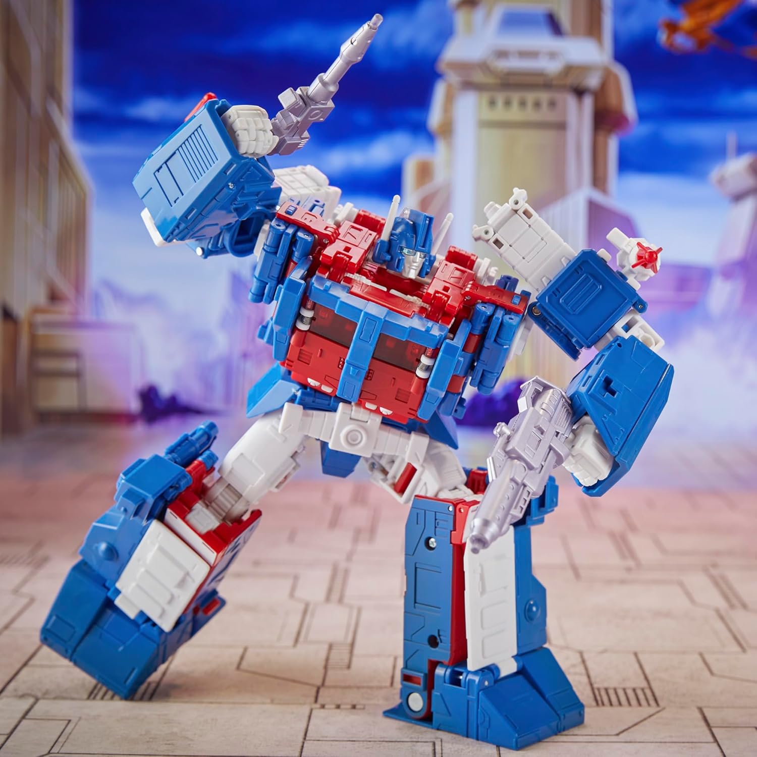 Transformers Ultra Magnus action figure in blue, red, and white posed with weapons on city background