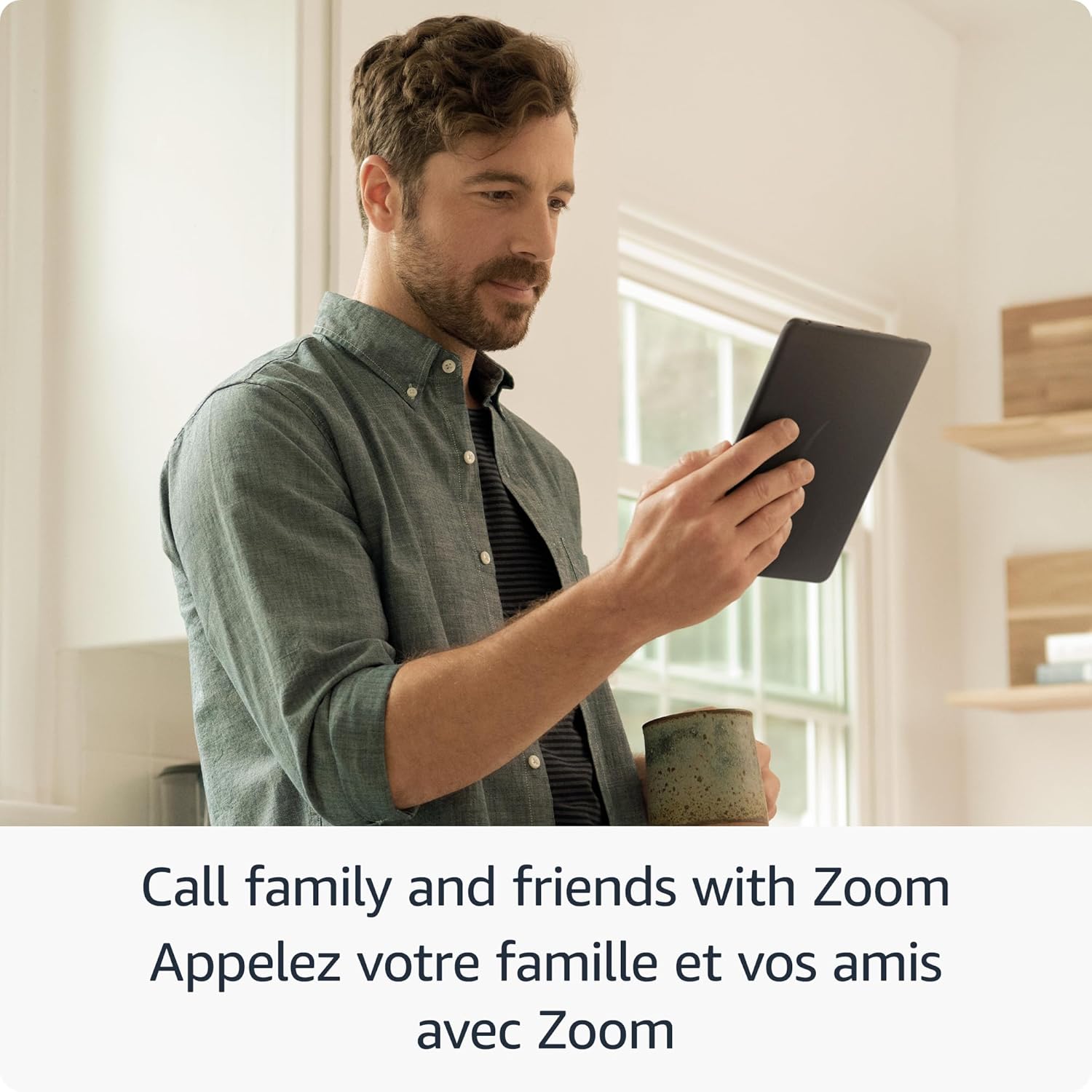 Man holding Amazon Fire HD 8 tablet with coffee cup in hand using Zoom for video calls at home