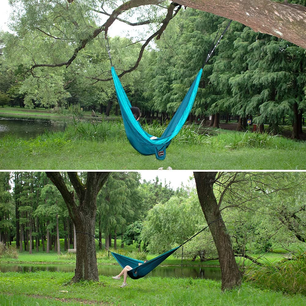 Lightweight camping hammock in blue by craques hanging between trees near a lake in a green forest