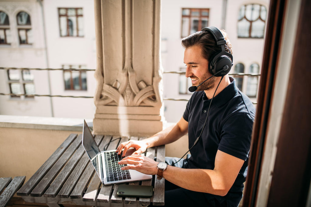 Man wearing beyerdynamic MMX 300 PRO gaming headset and using laptop at outdoor wooden table