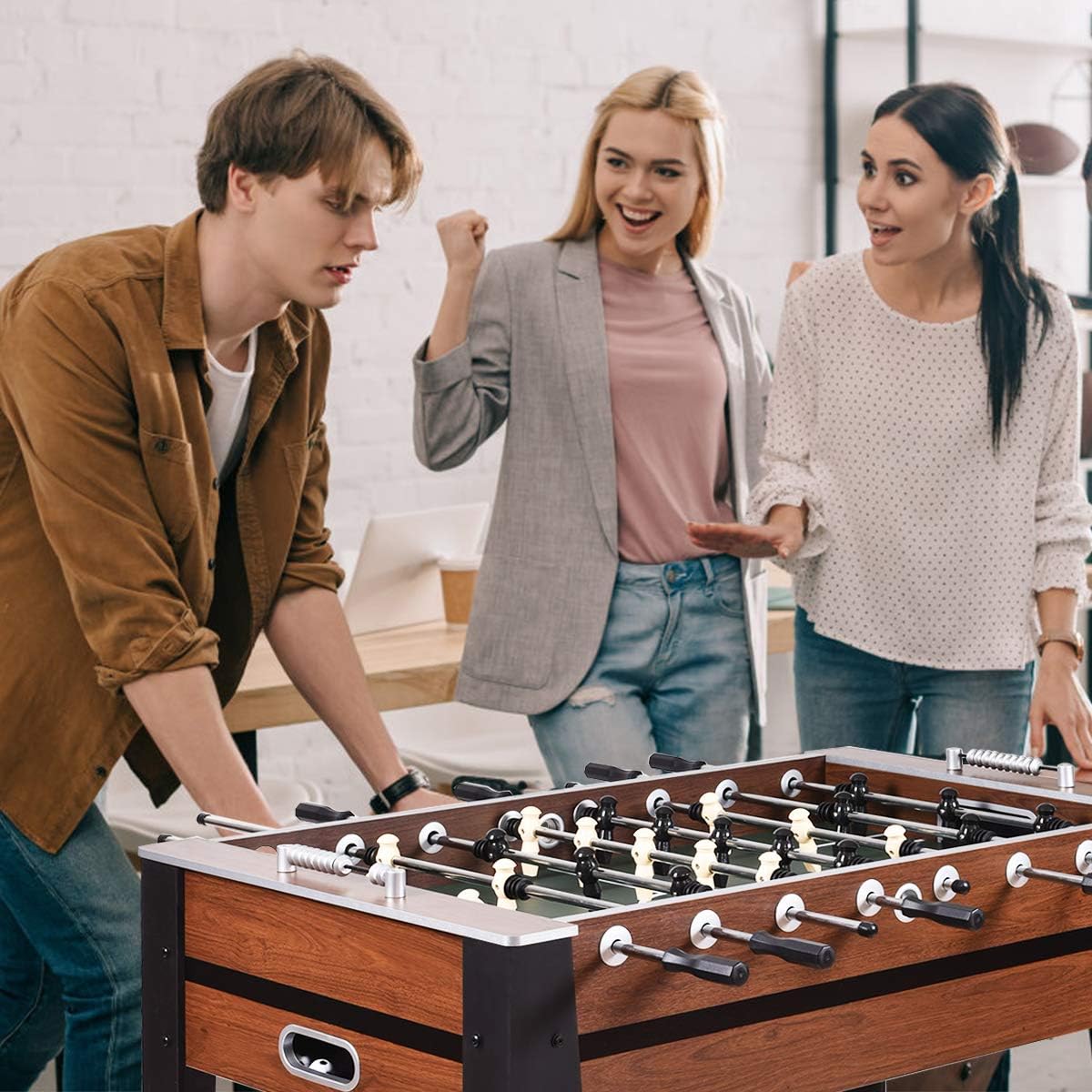 Three friends playing on a 54 inch foosball table with wooden finish and metal handles indoors