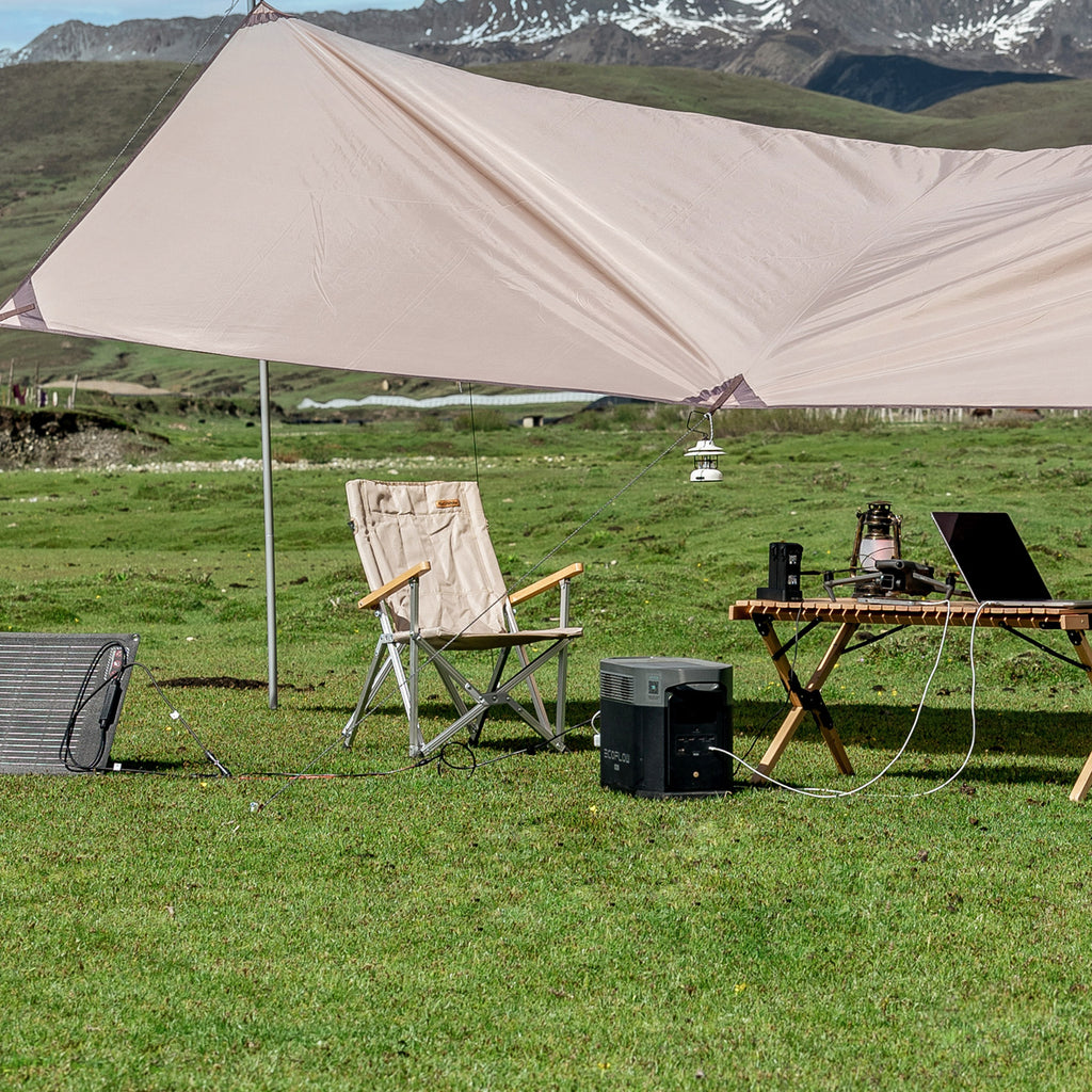 Craques portable solar generator kit powering laptop and lantern under camping tarp in mountain field