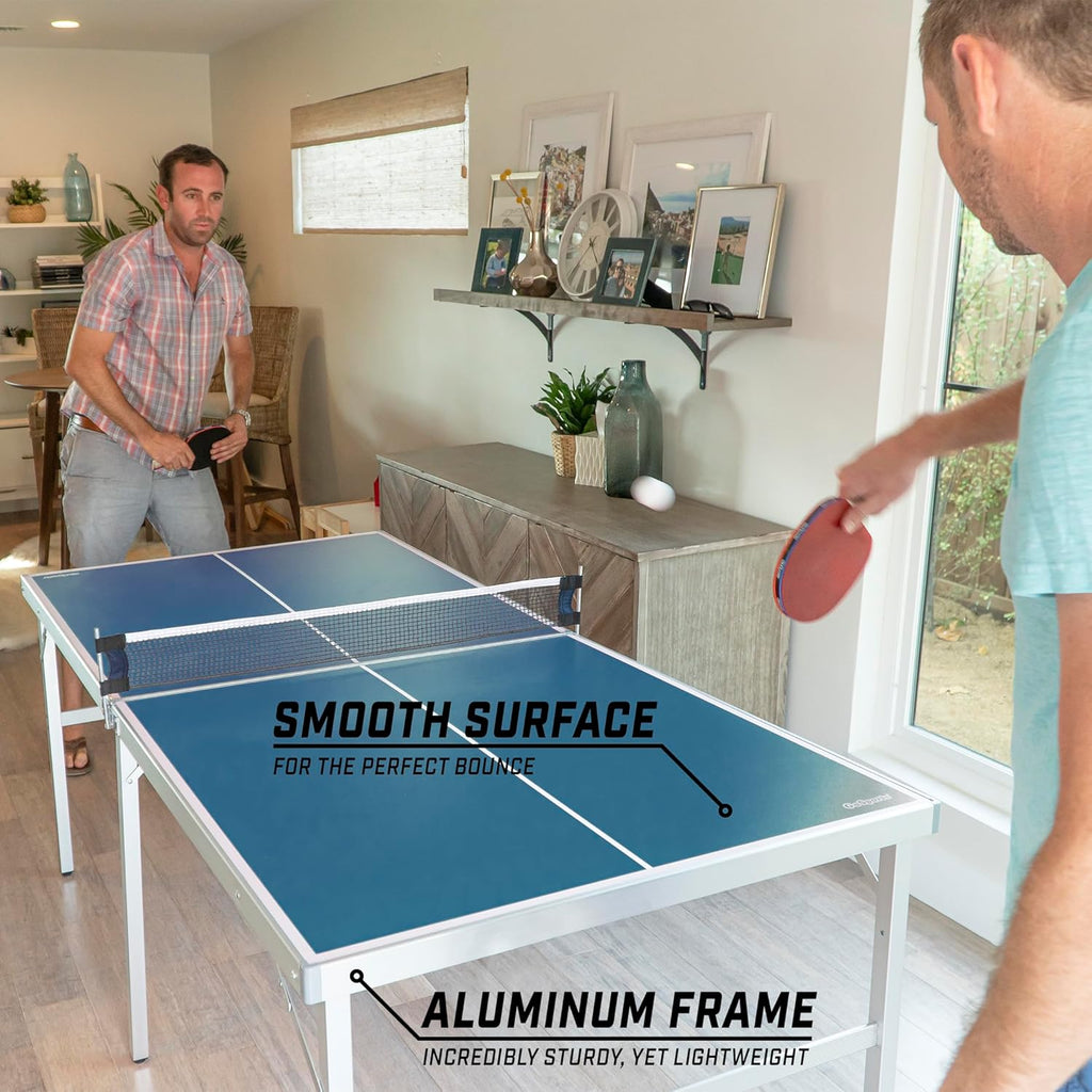 Two men playing on a portable table tennis set with a smooth blue surface and aluminum frame indoors