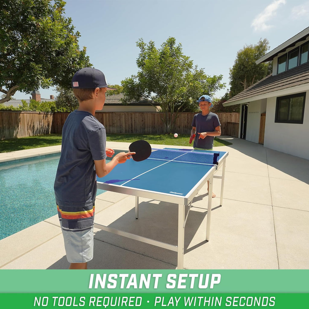 Two boys playing on a blue portable table tennis set outdoors next to a pool in a backyard