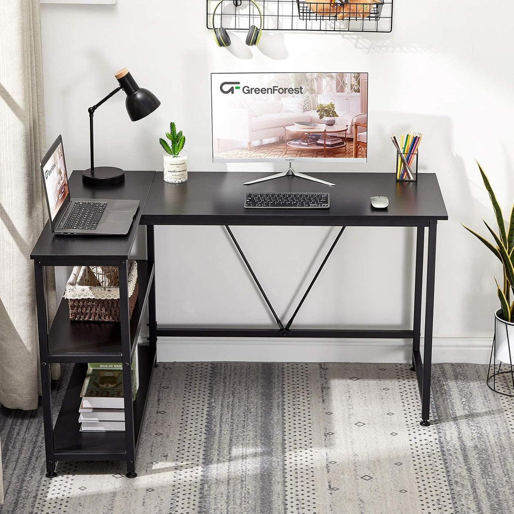 Black L shaped gaming desk with shelves featuring a laptop, monitor, desk lamp, and plant on top