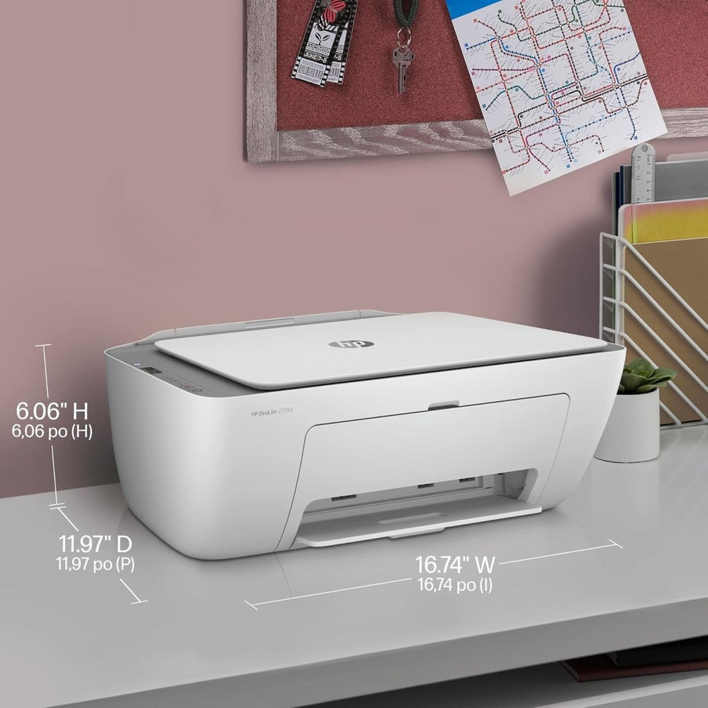 HP DeskJet 2855e wireless printer in white with dimensions shown on a desk near wall decor and office supplies