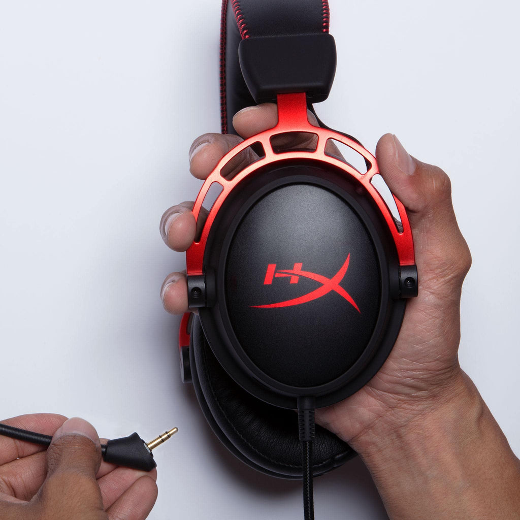 Hands holding a red and black HyperX Cloud Alpha gaming headset with detachable audio jack