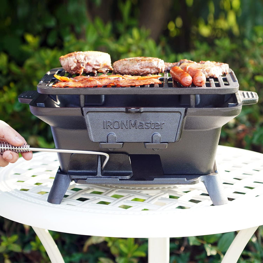 Portable cast iron bbq grill with burgers and sausages cooking on black IRONMaster grill outdoors