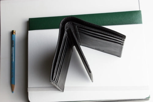 Open slim passcase wallet for men in black leather displayed on a desk with a notebook and pencil