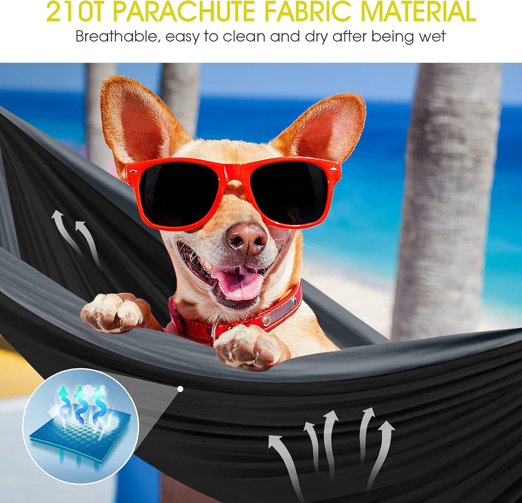 Dog wearing red sunglasses relaxing in black double camping hammock with ropes on beach