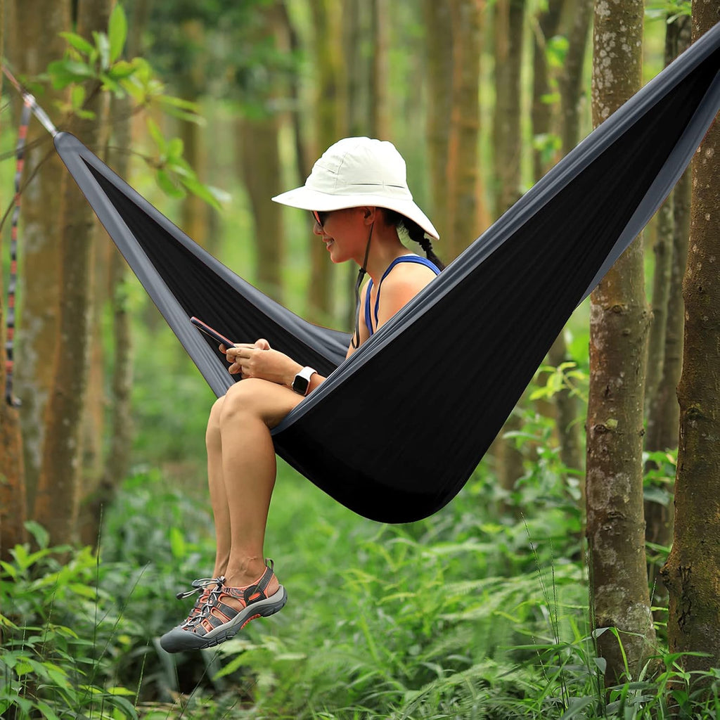 Craques double camping hammock with ropes in black hanging between trees with person sitting outdoors