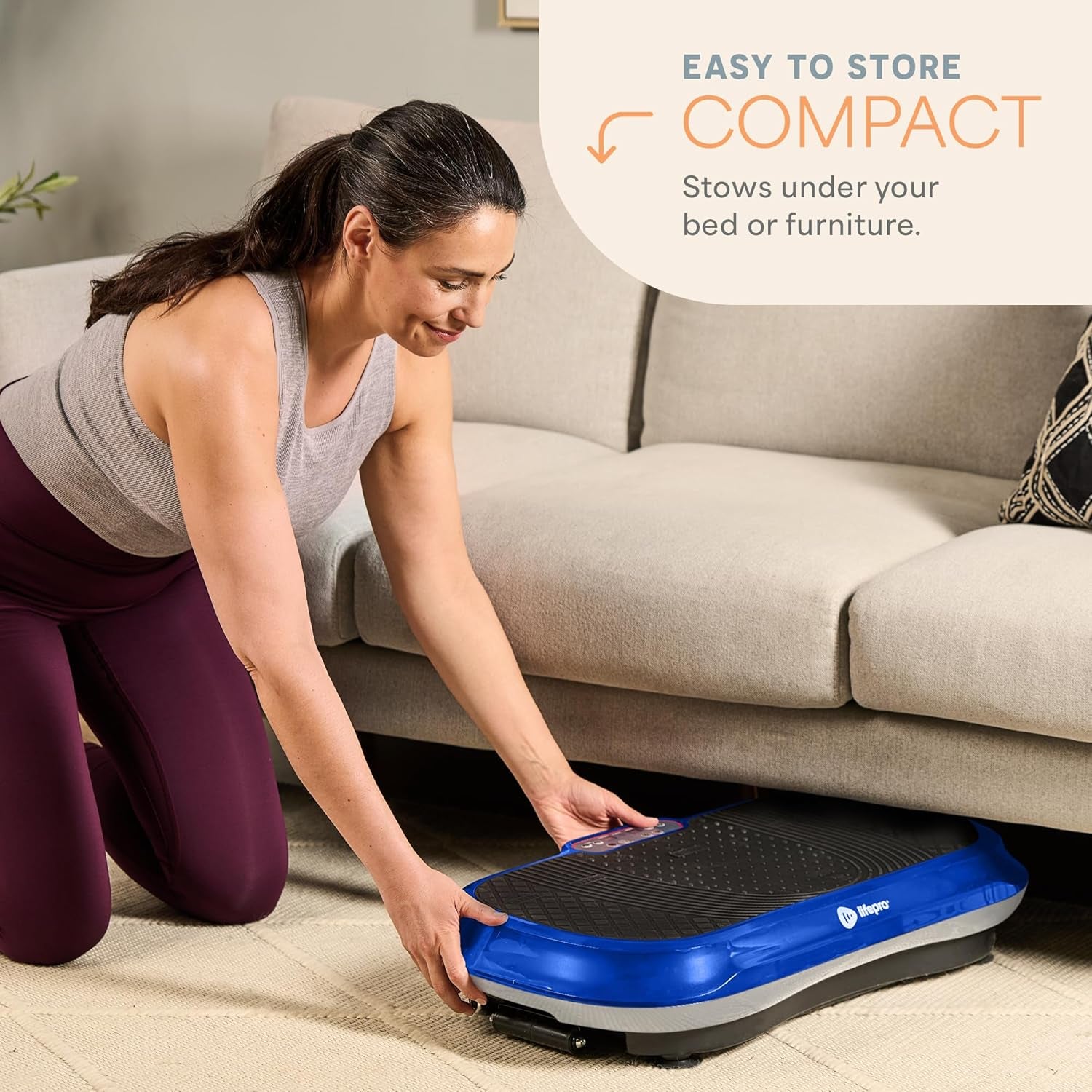 Woman storing compact craques vibration plate exercise machine under couch for easy home fitness