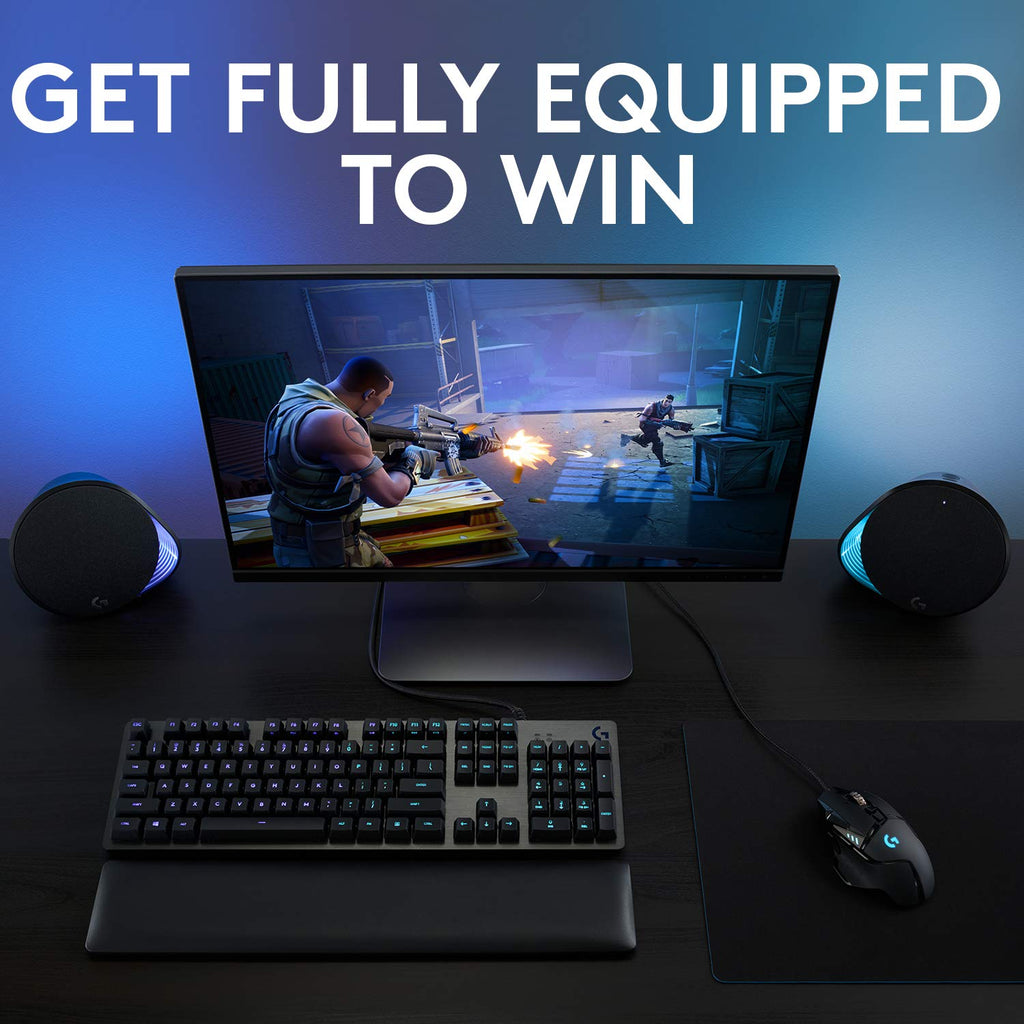 Logitech G502 HERO gaming mouse on black mousepad next to keyboard and monitor displaying shooter game