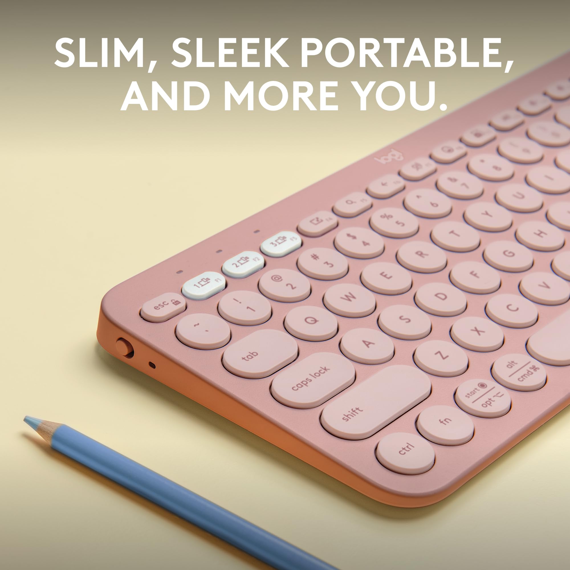 Close-up of pink Logitech Pebble Keys 2 K380s wireless keyboard with round keys next to a blue pencil