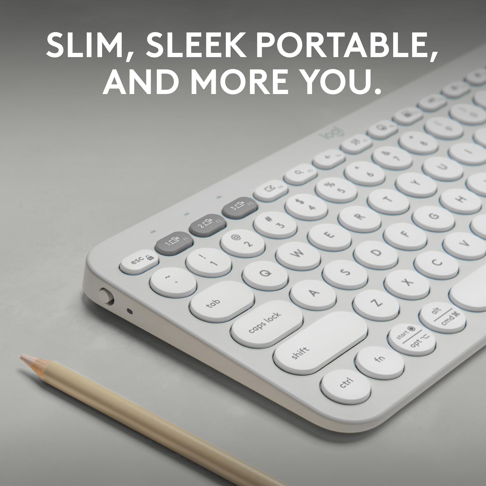 Close-up of Logitech Pebble Keys 2 K380s wireless keyboard in white with round keys and slim design next to a pencil