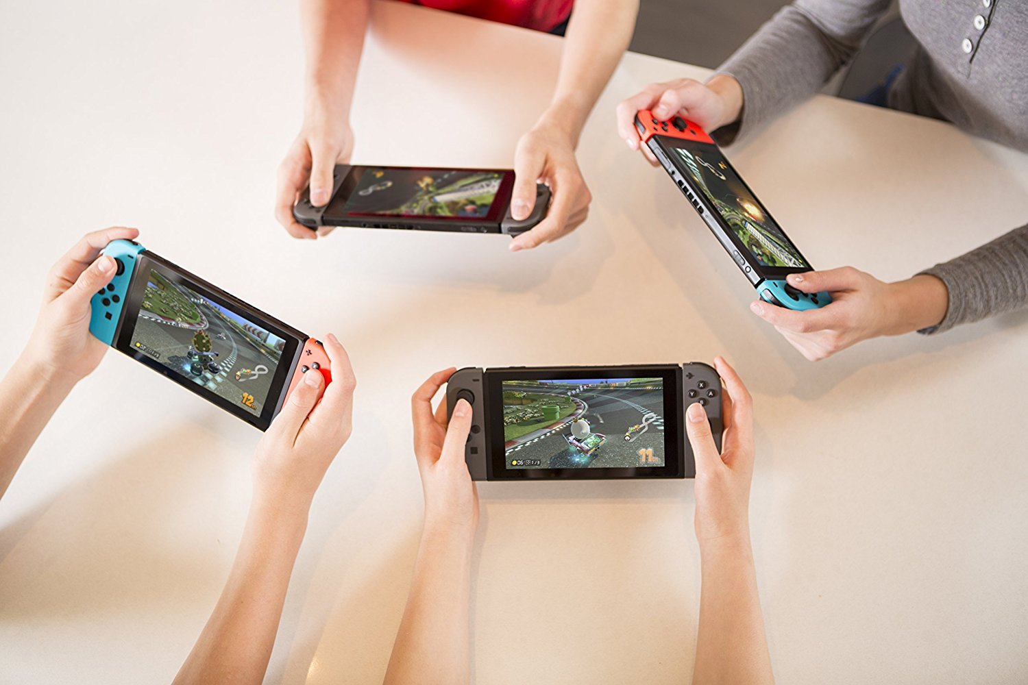 Four people playing Mario Kart 8 Deluxe Nintendo Switch on handheld Nintendo Switch consoles on a white table