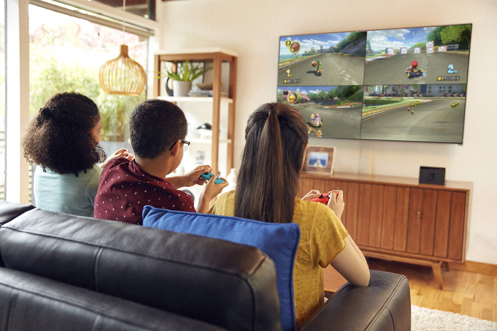 Three people playing Mario Kart 8 Deluxe Nintendo Switch on a wall-mounted TV in a living room