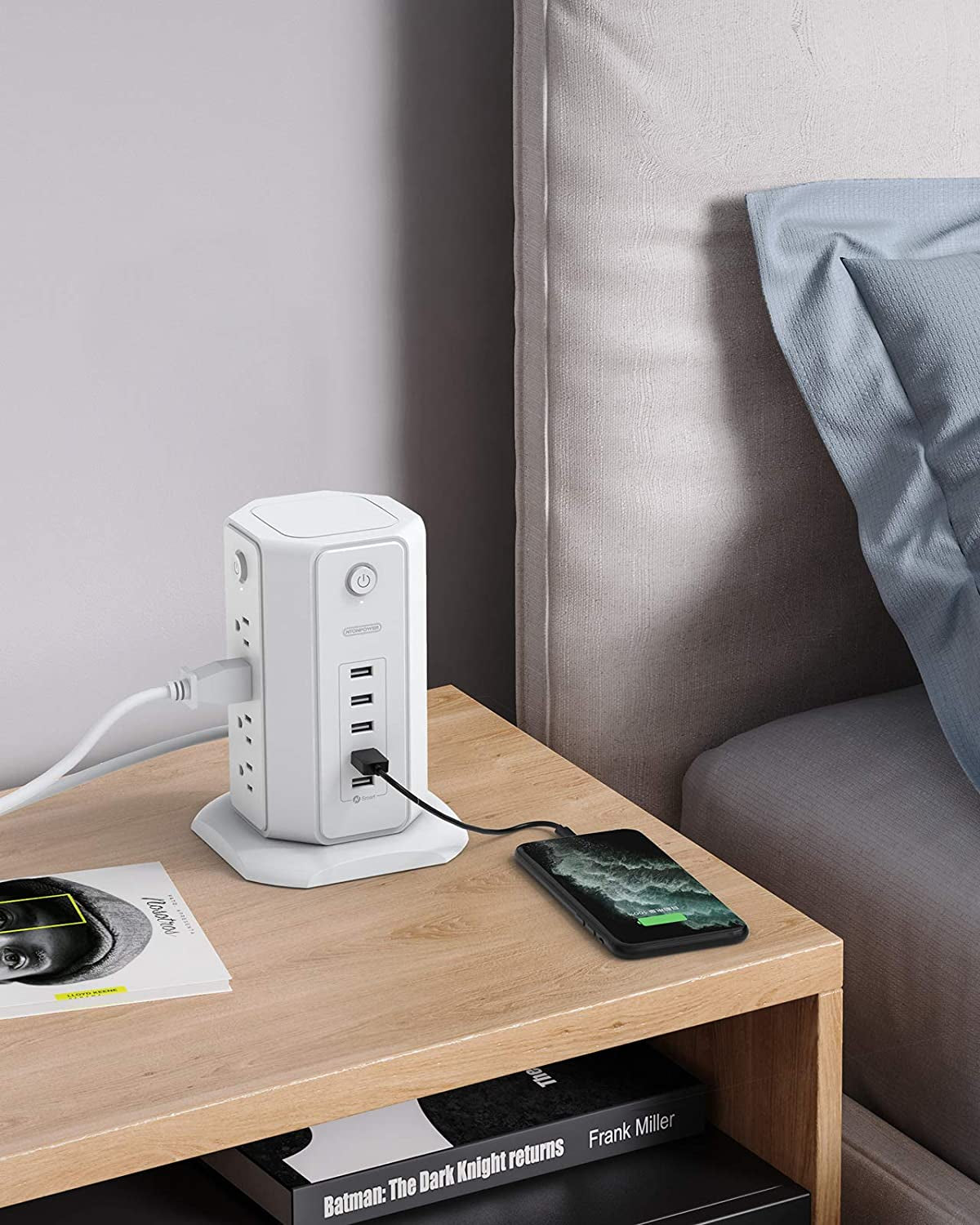 Craques white power strip tower with USB charging ports on bedside table next to a charging smartphone