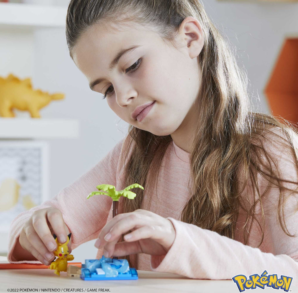 Girl assembling a Pokemon building toy kit featuring Pikachu and a palm tree on a blue base
