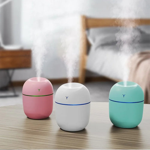 Three stylish portable ultrasonic humidifiers in pink, white, and green on a table with mist rising