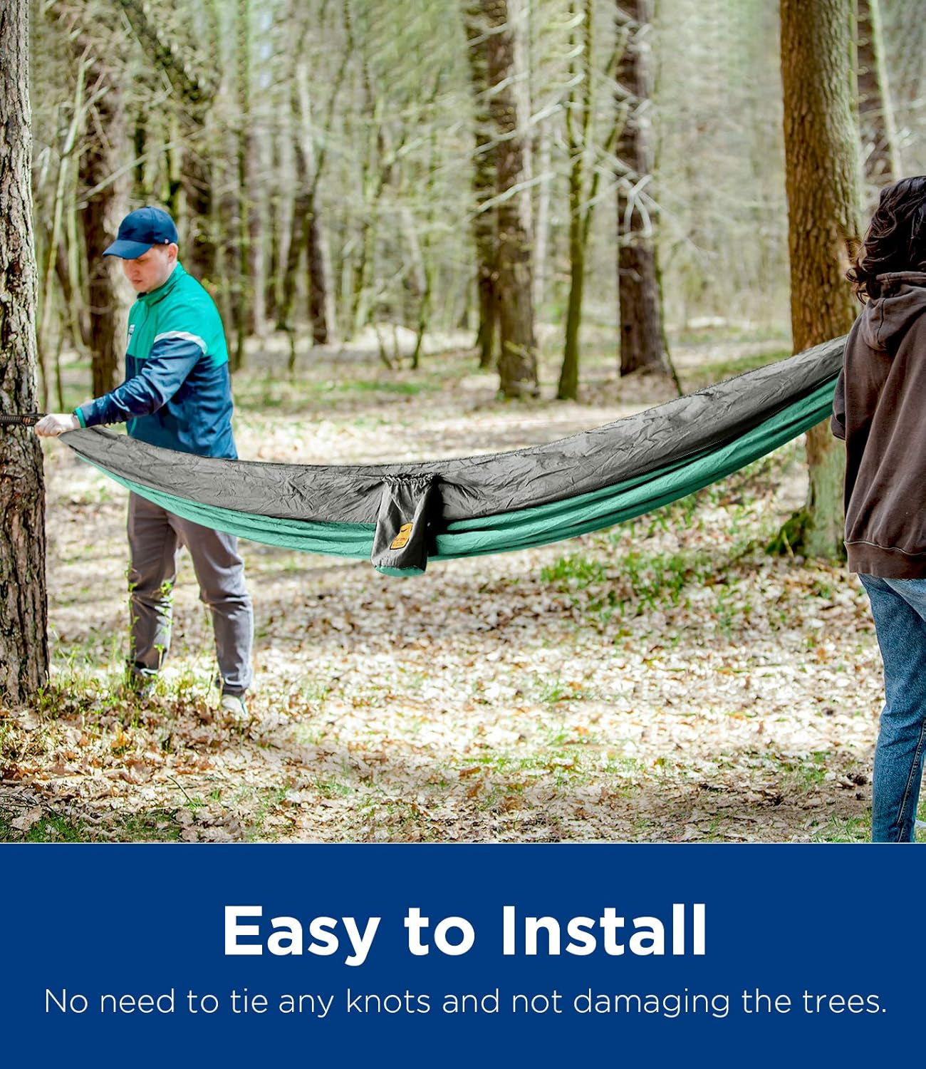 Two people setting up a gray and green ultralight camping hammock between trees in a forest