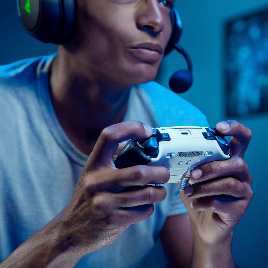 Person playing video games using Razer Wolverine V2 Pro PS5 controller with headset in a dim room
