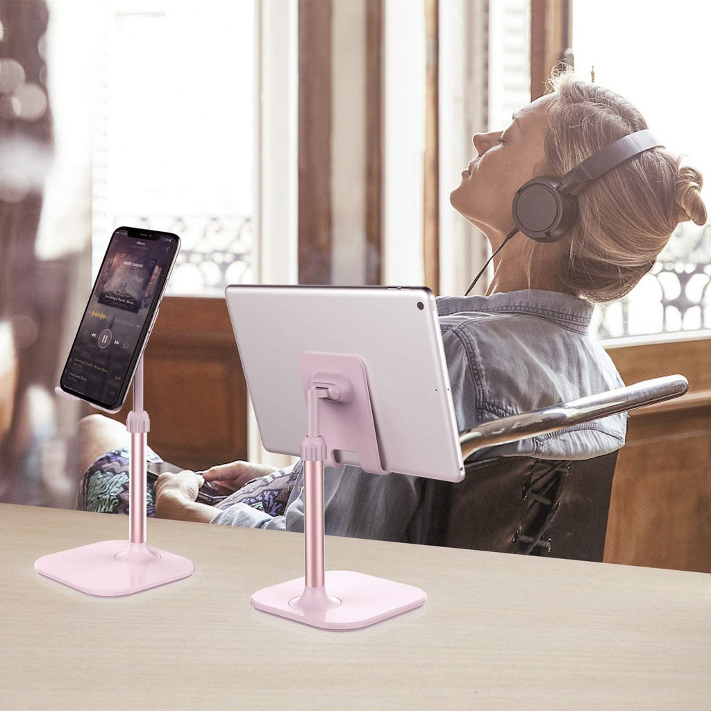 Pink adjustable cell phone stand for desk holding a phone and tablet with woman wearing headphones in background