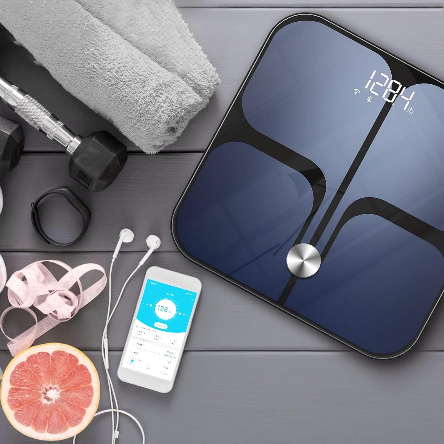 Black smart digital body fat scale with digital display placed next to fitness accessories and smartphone