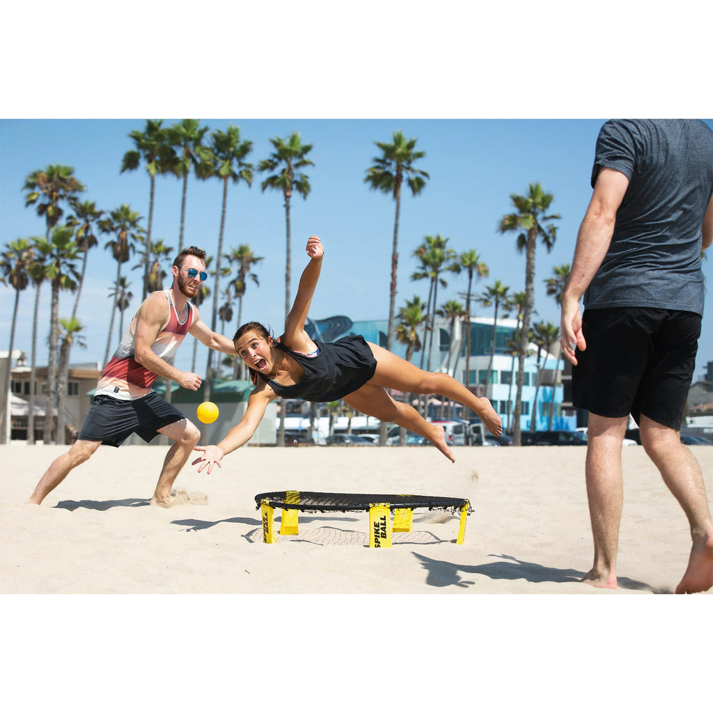 People playing Spikeball game set on a sandy beach with palm trees in the background